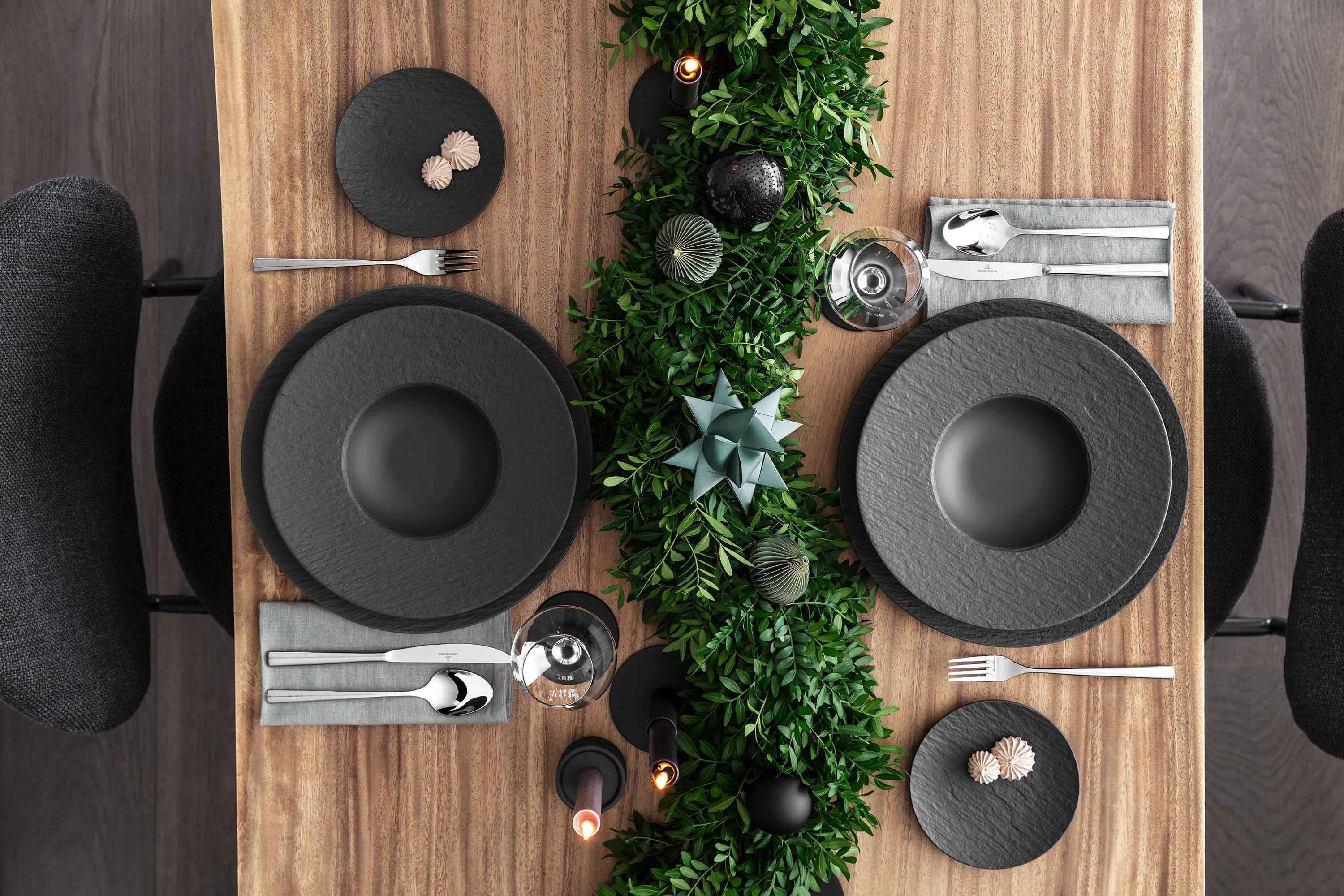 Elegant Christmas table with black Manufacture plates Elegant Christmas table with black Manufacture plates, cutlery and dark green festive decorations on a wooden table.
