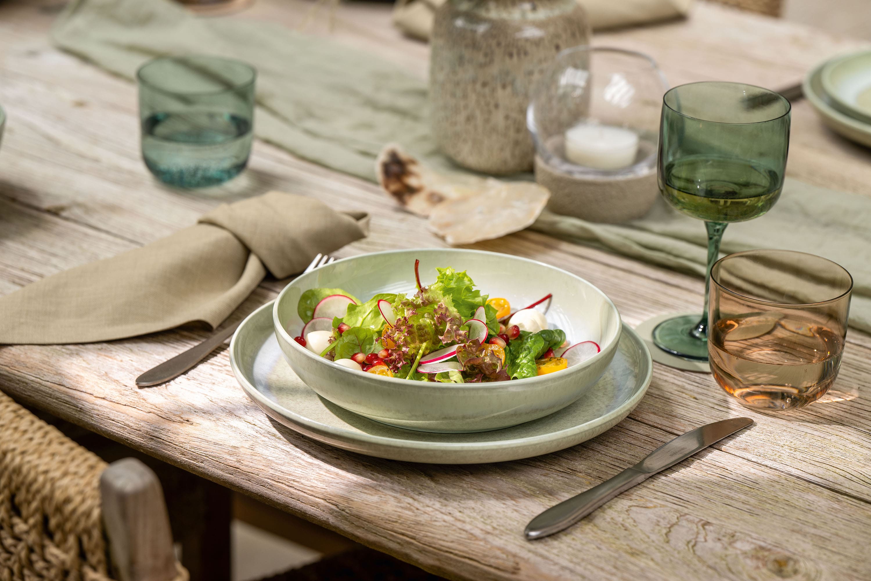 Un cuenco de ensalada Perlemor sobre una mesa de comedor puesta Un saladier trône sur une table dressée avec des verres, des assiettes et des serviettes beiges Perlemor.