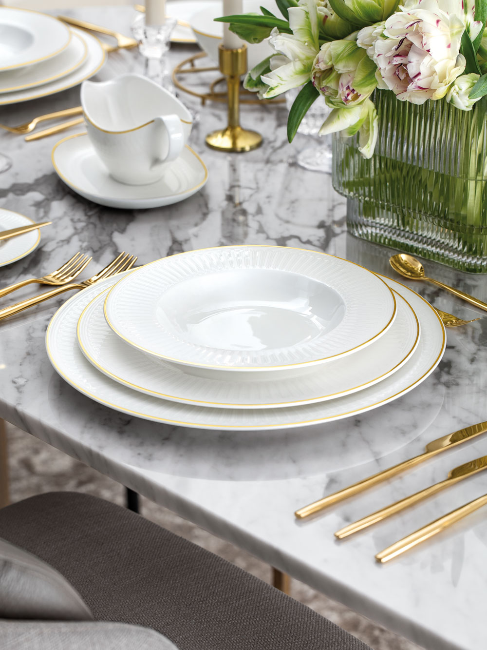 Château Septfontaines sur une table Un service de table formel avec des assiettes blanches, des couverts en or, une saucière blanche et une composition florale sur une table en marbre.