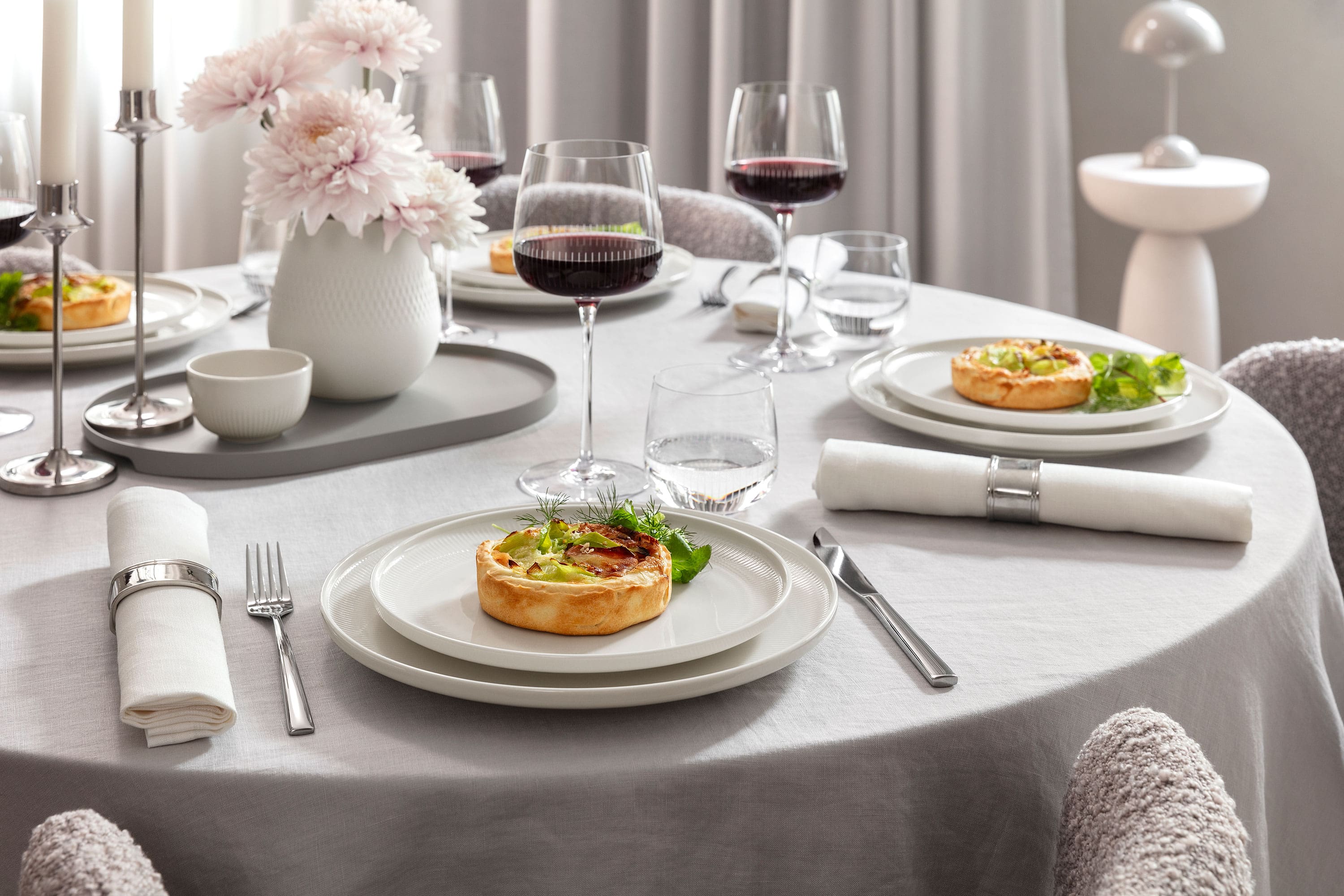 Elegant table set for four featuring Afina porcelain dinnerware and Maxima red wine glasses filled with wine. Served with food in a refined, modern dining atmosphere.